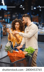 Young couple comparing items on a shopping list with products in their cart while walking through a supermarket aisle