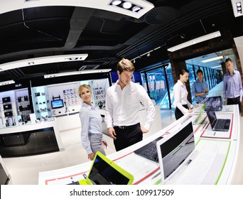 Young Couple In Consumer Electronics Store Looking At Latest Laptop, Television And Photo Camera