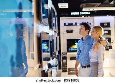 Young Couple In Consumer Electronics Store Looking At Latest Laptop, Television And Photo Camera