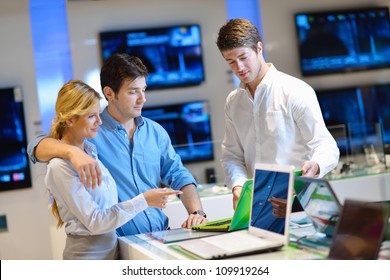 Young Couple In Consumer Electronics Store Looking At Latest Laptop, Television And Photo Camera