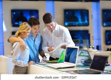 Young Couple In Consumer Electronics Store Looking At Latest Laptop, Television And Photo Camera