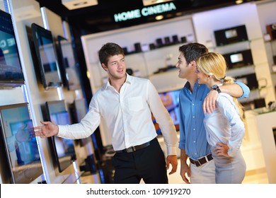 Young Couple In Consumer Electronics Store Looking At Latest Laptop, Television And Photo Camera