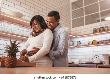 Young couple cooking together in the kitchen while man embracing his pregnant wife. Happy young couple cooking food at home, chopping vegetable on kitchen counter. - Powered by Shutterstock