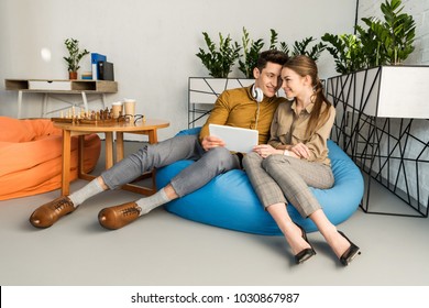 young couple cuddling using tablet together while sitting in bean bag