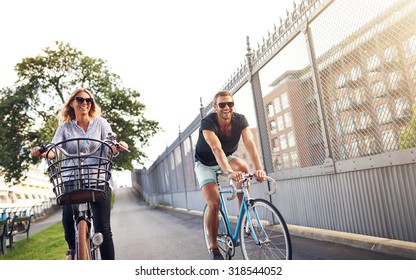 Young Couple Cycling In An Urban Park As They Enjoy A Healthy Outdoor Lifestyle In The Fresh Air And Summer Sun