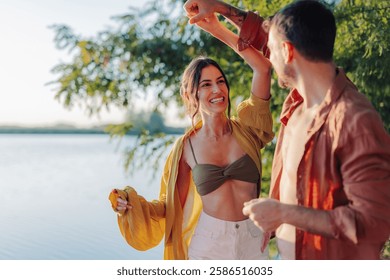Young couple dancing joyfully by the lake at sunset, embracing the warmth of summer holidays and creating unforgettable memories filled with love and happiness together