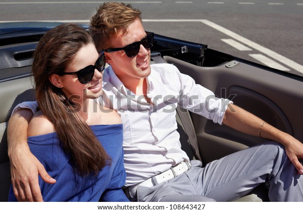 Young couple in dark sunglasses sits having\
embraced in a cabriolet on back\
seats