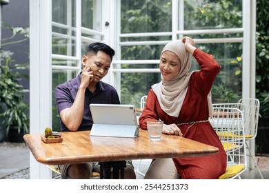 Young couple is deeply engaged in discussion while using a tablet at an outdoor cafe. The setting is casual and the atmosphere is collaborative, indicating a thoughtful brainstorming session. - Powered by Shutterstock