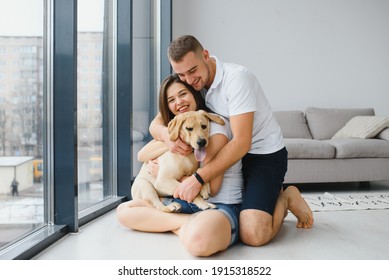 Young Couple With A Dog At Home. Young Man And A Woman Playing At Home With Dog.