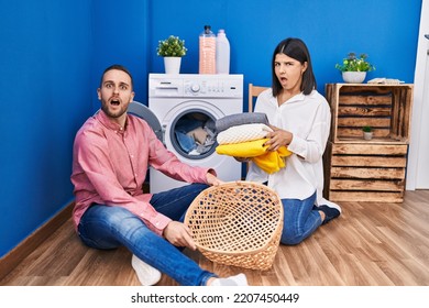 Young Couple Doing Laundry At Home In Shock Face, Looking Skeptical And Sarcastic, Surprised With Open Mouth 