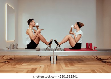 A young couple doing pilates on a reformer and drinking coffee from white coffee cups, group pilates training in a studio with a reformer, sports and leasure - Powered by Shutterstock