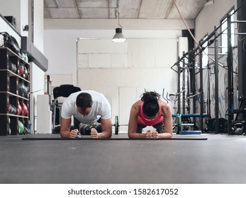 Young Couple Doing Planks At An Empty Crossfit Gym. Front Low Angle View.