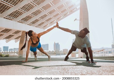 Young couple doing pushups outdoors. Beautiful woman exercising with her attractive personal trainer.