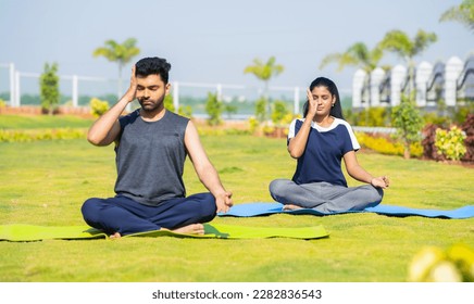 Young couple doing yoga or pranayama with eyes closed during morning at park - concept of healthy lifestyles, mindfulness and morning rituals - Powered by Shutterstock