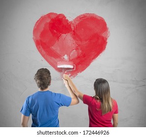 Young Couple Drawing A Big Heart In A Wall