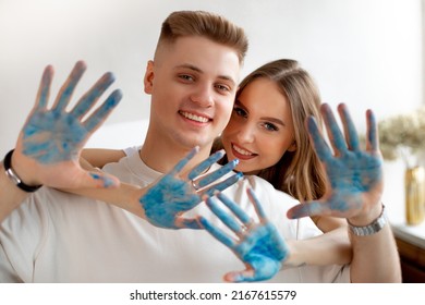 Young Couple Drawing Together. Woman And Man Looking At Camera And Show Blue Painted Palms.