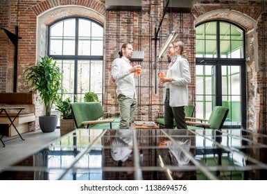 Young couple dressed in white standing together with drinks during the conversation in the beautiful spacious loft interior - Powered by Shutterstock