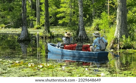 Young Couple Drifting in Boat and Photographing a Beautiful Cypress Swamp; Moncks Corner, South Carolina.