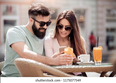 Young couple drinking coffee at cafe.They are smiling, looking at smart phone and drink juice.