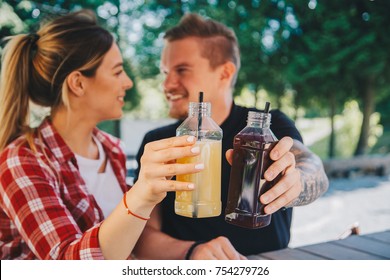 Young couple drinking healthy detox juice from plastic bootles outdoors in cafe. Close up. Fruit and vegetables pressed juice - Powered by Shutterstock