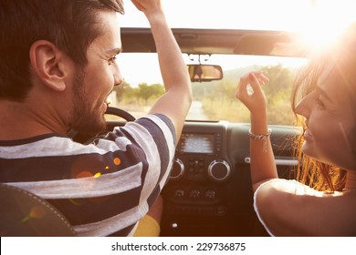 Young Couple Driving Along Country Road In Open Top Car