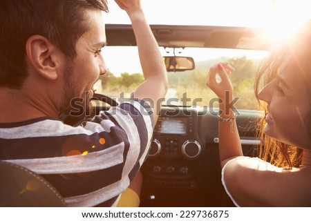 Young Couple Driving Along Country Road In Open Top Car