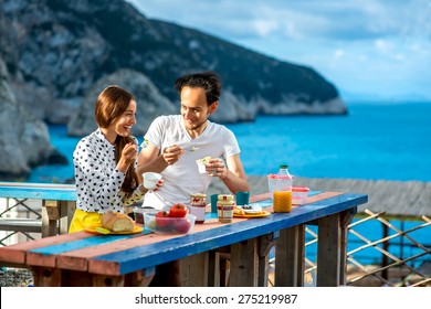 Young Couple Eating Breakfast On The Table Near The Sea On Their Summer Vacation