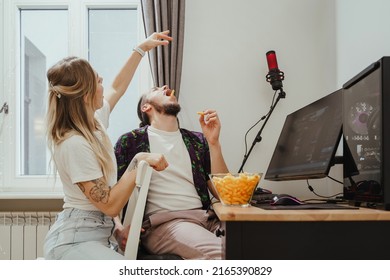 Young Couple Eating Cheese Puffs While Playing Video Games Or Watching Something Online At Home