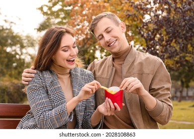 Young Couple Eating French Fries In Park