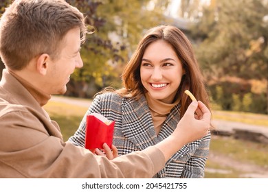 Young Couple Eating French Fries In Park