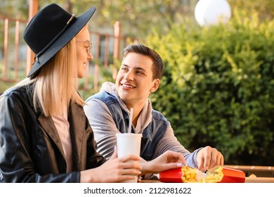 Young Couple Eating French Fries In Cafe Outdoors