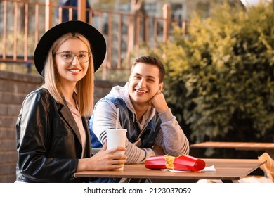 Young Couple Eating French Fries In Cafe Outdoors