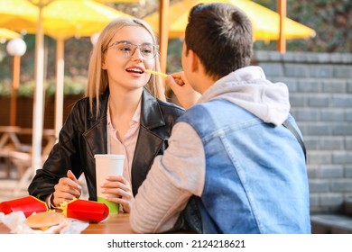 Young Couple Eating French Fries In Cafe Outdoors