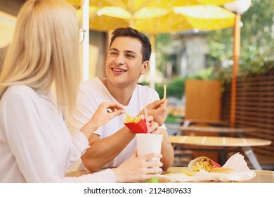 Young Couple Eating French Fries In Cafe Outdoors