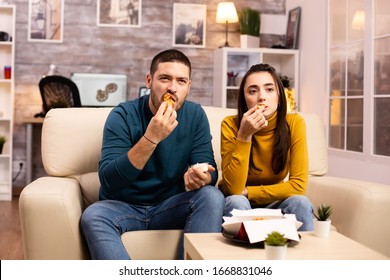 Young Couple Eating Fried Chicken In Front Of The TV In The Living Room