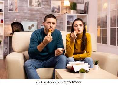 Young Couple Eating Fried Chicken In Front Of The TV In The Living Room