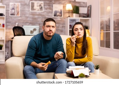 Young Couple Eating Fried Chicken In Front Of The TV In The Living Room