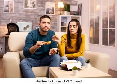 Young Couple Eating Fried Chicken In Front Of The TV In The Living Room