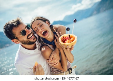 Young couple eating fruit on the beach- summer party with friends and healthy food concept. Selective focus. - Powered by Shutterstock