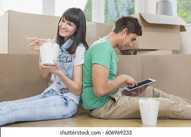 Young Couple Eating Noodle And Using Digital Tablet In Their New House