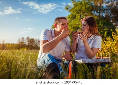 Young Couple Eating Pizza Outside. Woman And Man Having Picnic At Sunset. Fast Food Concept.