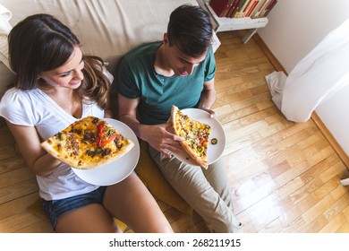 Young Couple Eating Pizza.They Sitting On Floor And Joying In Hot Pizza.Image Taken From Above.