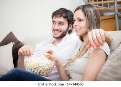 Junge Ehepaare, die Popcorn essen, während sie sich einen Film ansehen