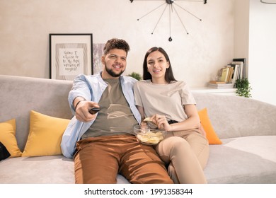 Young Couple Eating Potato Chips And Watching Tv On Couch In Living-room