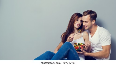 Young couple eating salad together. Vegetarian, weight lossing, dieting, healthy food concept, against grey background, with copyspace for slogan or text message.  Horizontal banner composition.