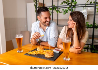 Young Couple Eating Take Away Food At Home, Having Burgers And Beer For Lunch