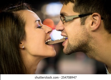 Young Couple Eating Together One Piece Of Chocolate - In Street At Night