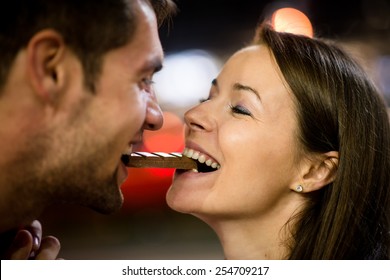 Young Couple Eating Together One Piece Of Chocolate - In Street At Night