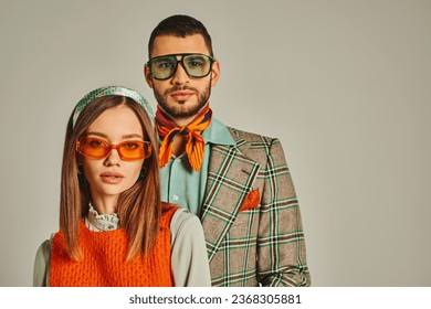 young couple in elegant vintage clothes and sunglasses looking at camera on grey, fashion from past - Powered by Shutterstock