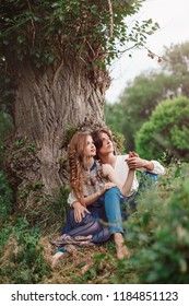 Young Couple Of Elves In Love Sitting In Magical Forest Agaist The Big Tree Outdoor On Nature. Fairy Tale Of Love, Relationship And Magik People Concept. Man Ambracing Woman